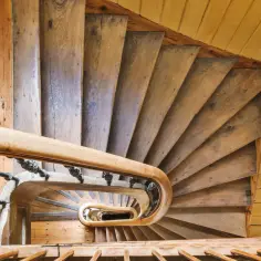 Kręcone drewniane schody do domu, z ozdobną balustradą, prowadzą w dół.