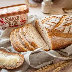 Chleb bezglutenowy pokrojony w kromki, z masłem i opakowaniem Smako Wita w tle.