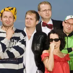 Kabaret Moralnego Niepokoju członkowie pozują do zdjęcia na tle nieba. Widać ich w różnych strojach, od sportowych po eleganckie.
