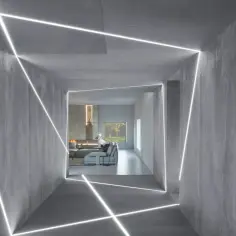 Nowoczesny korytarz z betonowymi ścianami, w których biegnie geometryczna listwa LED, tworząc futurystyczny efekt.