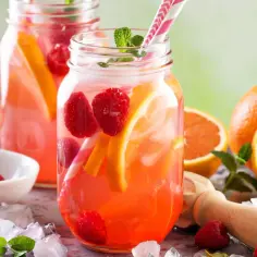 Orzeźwiający drink z malinami, pomarańczą i miętą w słoiku, obok świeżych owoców i lodu.
