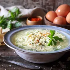 Zupa stracciatella z parmezanem i jajkami, ozdobiona natką pietruszki i papryką.