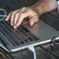 Dłoń na klawiaturze laptopa, obok biała filiżanka. Czas na szybkie rozwiązanie problemu: jak zrestartować laptopa.