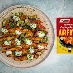 Pyszny kurczak gyros z warzywami i sosem na tortilli, obok paczka przyprawy Prymat Air Fryer.