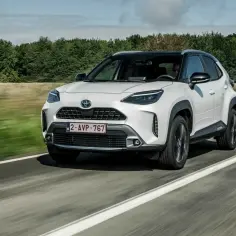 Biały Toyota Yaris Cross na drodze. Kierowca w okularach przeciwsłonecznych. Wiele osób szuka **toyota yaris cross opinie** przed zakupem.