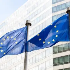 Flagi Unii Europejskiej powiewają przed nowoczesnym budynkiem, symbolizując jedność i współpracę krajów unii europejskiej.