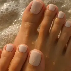Delikatne, jasne paznokcie u stóp z subtelną kropką – idealny modny pedicure na letnie dni, gdy stopy zanurzają się w morskiej pianie.