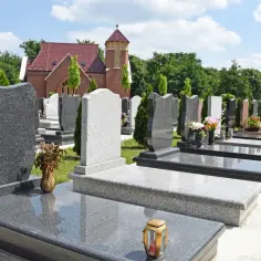 Cmentarz z rzędami nagrobków i budynkiem kościoła w tle.