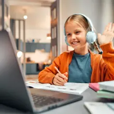 Uśmiechnięta dziewczynka w słuchawkach uczy się angielskiego online. Zastanawiasz się, ile zarabia korepetytor angielskiego?