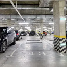 Wielopoziomowy parking podziemny z rzędami samochodów. Widoczne betonowe kolumny, oświetlenie i oznaczenia miejsc parkingowych, w tym numer 43.