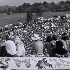 Tłum ludzi na festiwalu, gdzie jest Woodstock. Młodzi siedzą na ozdobionej ciężarówce, patrząc na scenę.