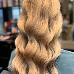 Lśniące, falowane blond włosy po zabiegu olejowania. Włosy wyglądają zdrowo i są pełne blasku.