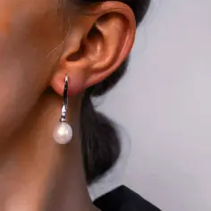 Eleganckie kolczyki z perłą, wiszące przy uchu. Delikatny piercing podkreśla piękno biżuterii.