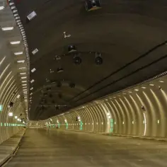 Nowy tunel na Zakopiance, oświetlony rzędem zielonych świateł i lamp, z widocznym żółtym pojazdem budowlanym.