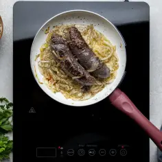 Kaszanka z patelni smaży się z cebulką. Obok czosnek, pieprz i natka pietruszki.