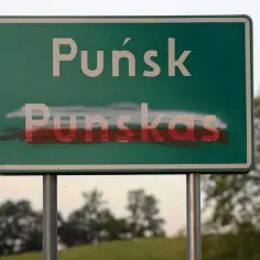 Znak drogowy z napisem "Puńsk" i "Punskas", częściowo zamalowany czerwoną farbą, symbolizuje napięcia związane z mniejszością narodową.