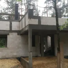 Budowa domu w lesie. Widoczne białe bloczki, betonowe słupy i trzpienie żelbetowe w ścianach murowanych.