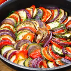 Ratatouille, charakterystyczne potrawy kuchni francuskiej, w naczyniu z warzywami: cukinią, bakłażanem, pomidorem i cebulą, przybrane ziołami.