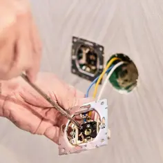 Ręce majsterkowicza montują mechanizm włącznika, przygotowując instalację, jak podłączyć światło na dwa włączniki.