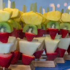 Kolorowe szaszłyki owocowe dla dzieci: ananas, kiwi, truskawki i melon. Idealna przekąska na przyjęcie.