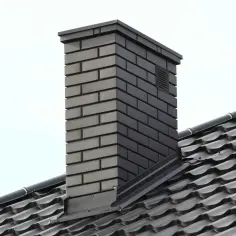 Nowy komin z cegły z okapem z blachy, chroniącym przed deszczem. Dach pokryty ciemną dachówką.