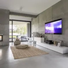 Nowoczesny salon z betonowymi ścianami, kominkiem i dużym telewizorem 70 cali. Wymiary tego ekranu robią wrażenie!