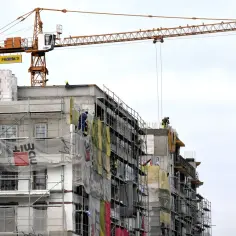 Budowa domu to inwestycja, która może przynieść zyski. Na placu budowy widać dźwig i robotników.