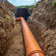 Instalacja kanalizacyjna w wykopie. Pomarańczowa rura 110 mm z minimalnym spadkiem prowadzi do studzienki.