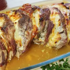 Karkówka pieczona w plastrach z cebulą, zapieczona z serem, w szklanym naczyniu, z sosem i natką pietruszki.