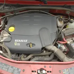 Silnik 1.5 dCi pod maską czerwonego samochodu. Widoczny jest czarny plastikowy dekiel silnika z napisem Renault, akumulator i inne elementy komory silnika.