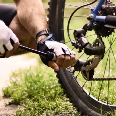 Rowerzysta w rękawiczkach pompuje koło roweru, pokazując, jak napompowac koła na stacji.