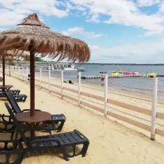 Słoneczna plaża nad Jeziorem Otmuchowskim, z leżakami, parasolami i kolorowymi rowerami wodnymi.