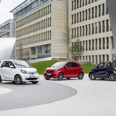 Trzy samochody Smart, w tym jeden w wersji Brabus, zaparkowane przed nowoczesnym budynkiem.