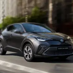 Ciemnoszary Toyota C-HR Hybrid porusza się po miejskiej ulicy, podkreślając jego dynamiczny design.