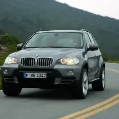 Szary BMW X5 E70 pokonuje zakręt na malowniczej górskiej drodze.
