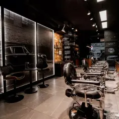 Stylowy salon fryzjerski z czarnymi fotelami, grafiką samochodu na ścianie i neonowym oświetleniem. Miejsce godne Franck Provost.