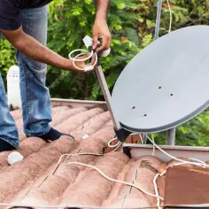 Instalator reguluje uchwyt anteny satelitarnej na dachu.