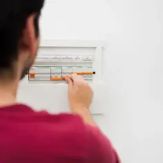 Mężczyzna manipuluje wyłącznikami w skrzynce elektrycznej, co może być pierwszym krokiem, by dowiedzieć się, jak obliczyć zużycie prądu.