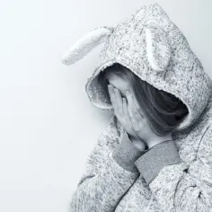 Dziewczynka w bluzie z uszami królika zakrywa twarz dłońmi, smutna. Może to być związane z elicea skutki uboczne.