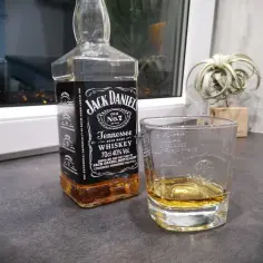 Butelka Jack Daniel's Tennessee Whiskey i szklanka z bursztynowym płynem. Idealny zestaw na wieczór.