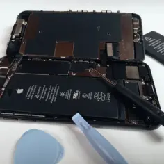 Rozłożony iPhone 8 z widoczną baterią i narzędziami do naprawy.