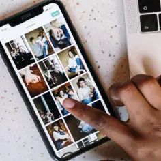 Palec dotyka ekranu telefonu z galerią zdjęć, pokazując jak przenieść zdjęcia z telefonu na pendrive. Obok leży laptop.