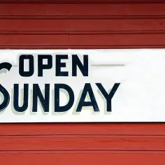 Tablica "OPEN SUNDAY" na czerwonej, drewnianej ścianie. To znak, że praca w niedziele jest możliwa.