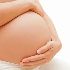Dłońmi obejmuje zaokrąglony brzuch, w którym dziecko ułożyło się w położenie podłużne główkowe.