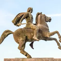 Pomnik Aleksandra Wielkiego na koniu, w zbroi i z mieczem, na tle błękitnego nieba.