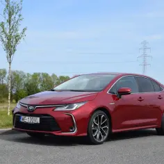 Czerwona Toyota Corolla 1.8 Hybrid zaparkowana na tle zieleni i błękitnego nieba.