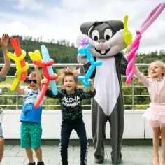 Dzieci z animatorami w strojach postaci z balonami w rękach, radośnie świętują, jakby to był ostatni dzień wakacji.
