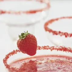 Truskawka na brzegu kieliszka z drinkiem, ozdobionym cukrem.