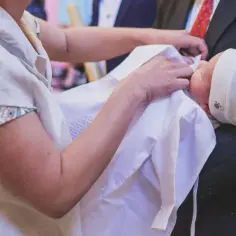 Dziecko w bieli otulone przez rodziców, symboliczne skutki przyjęcia chrztu.