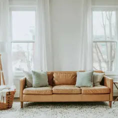 Przytulny salon z brązową kanapą, idealny do wynajem mieszkania. Jasne zasłony i duży dywan tworzą ciepłą atmosferę.